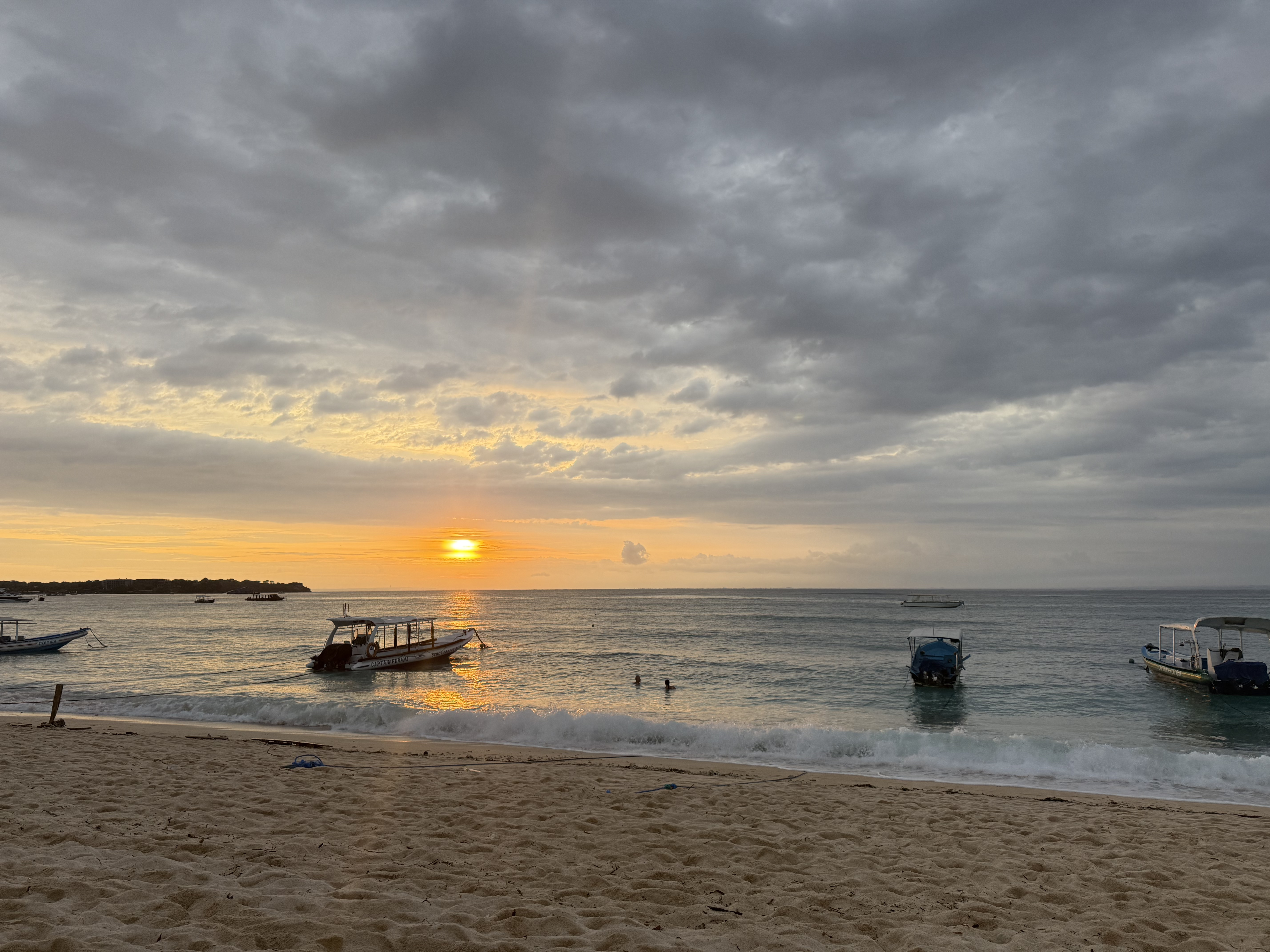 ボートが何艇も停泊している浜辺に夕陽が沈もうとしている様子