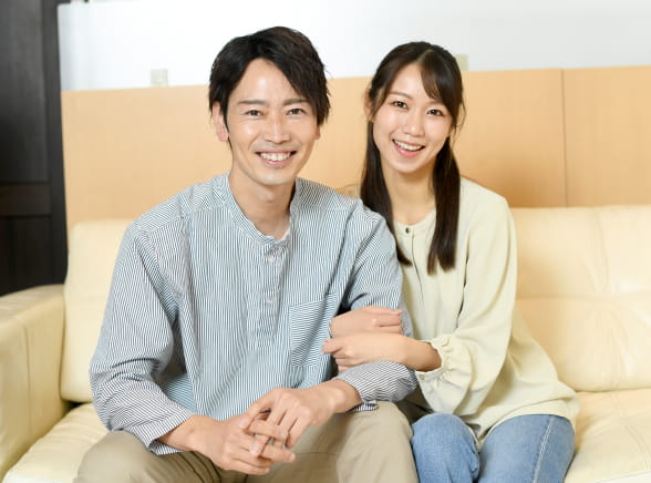 腕を組んだ30代カップルがソファーに座っている様子